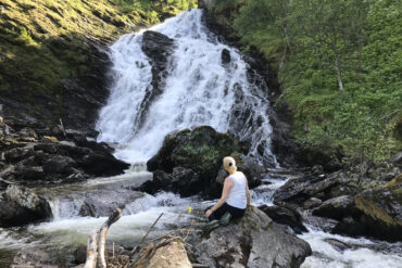 Person på stein med foss og grønn natur i bakgrunnen