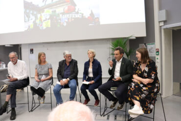 Panel av mennesker sitter på en scene under en storskjerm.